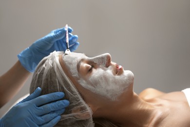 Photo of Cosmetologist applying mask on client's face in spa salon