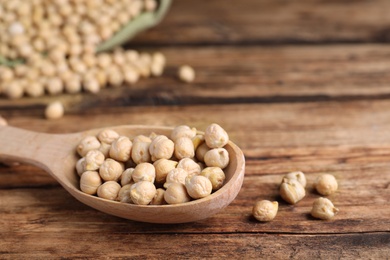 Photo of Spoon with chickpeas on wooden table, closeup. Space for text