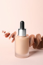 Bottle of skin foundation and decorative branch on beige background. Makeup product