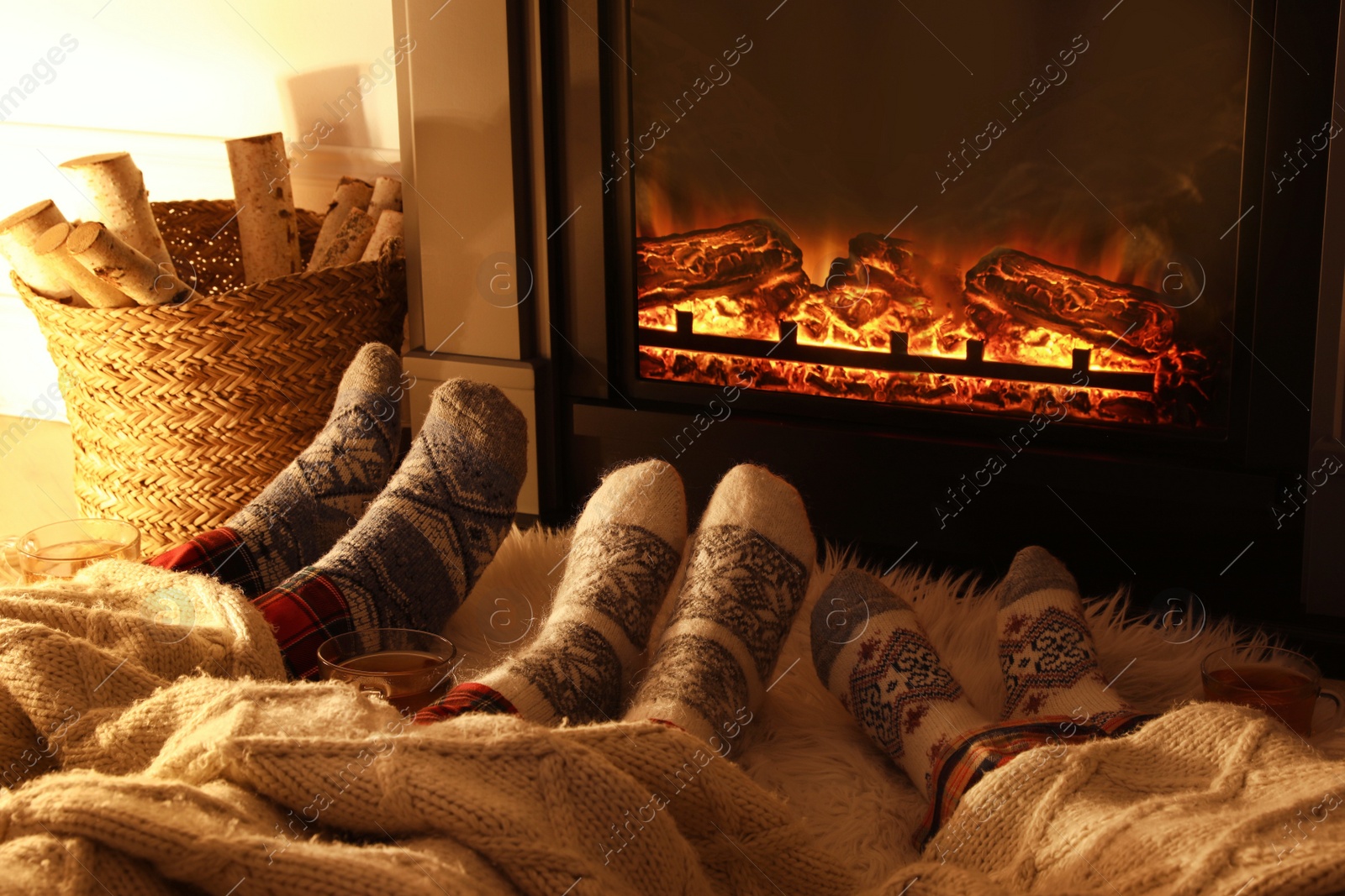 Photo of Family in warm socks resting near fireplace at home, closeup of legs