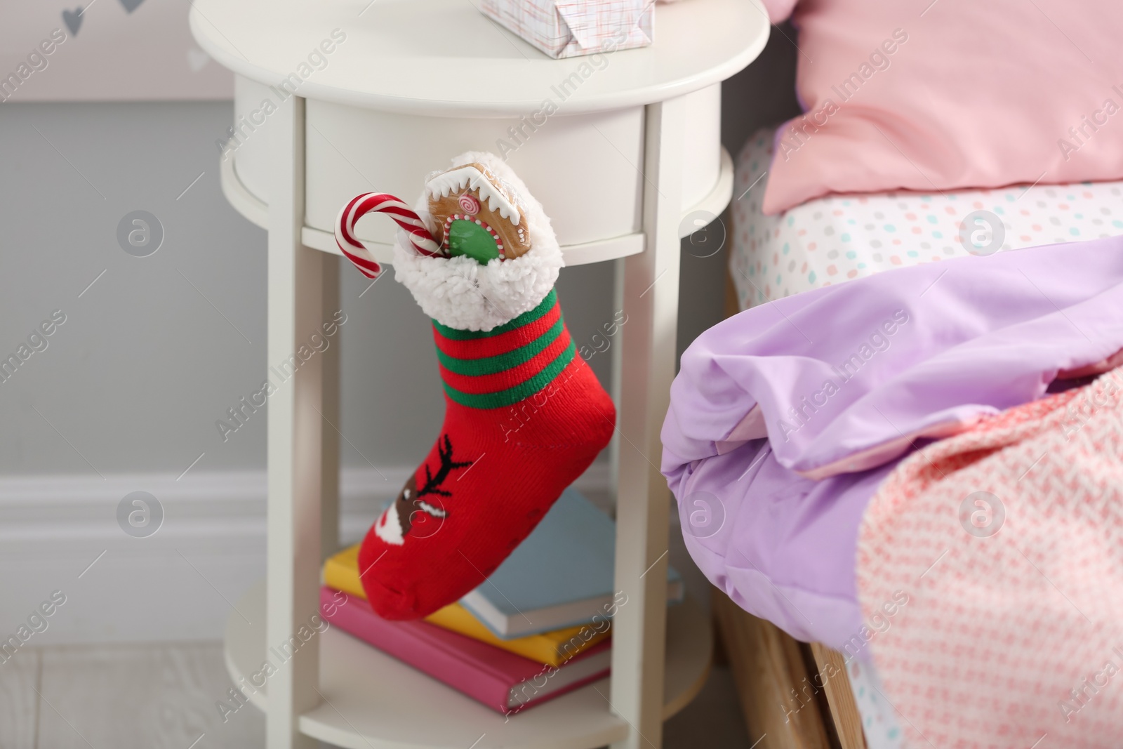 Photo of Stocking with presents hanging on white table in children's room, closeup. Saint Nicholas Day tradition