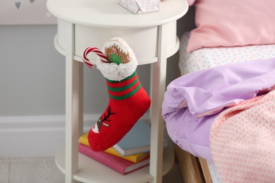 Photo of Stocking with presents hanging on white table in children's room, closeup. Saint Nicholas Day tradition