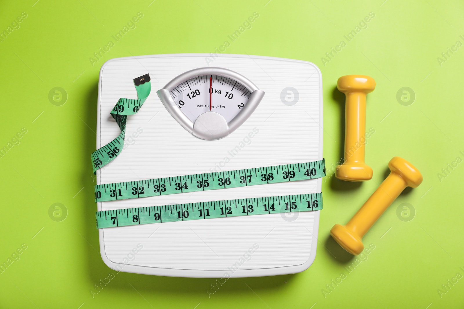 Photo of Weight loss concept. Scales, dumbbells and measuring tape on green background, flat lay