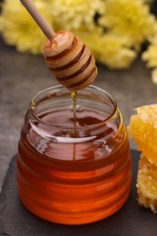 Photo of Pouring sweet golden honey from dipper into jar on grey table, closeup