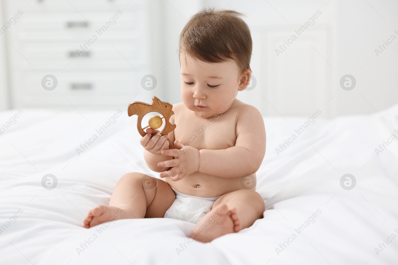 Photo of Cute baby boy with wooden rattle on bed at home