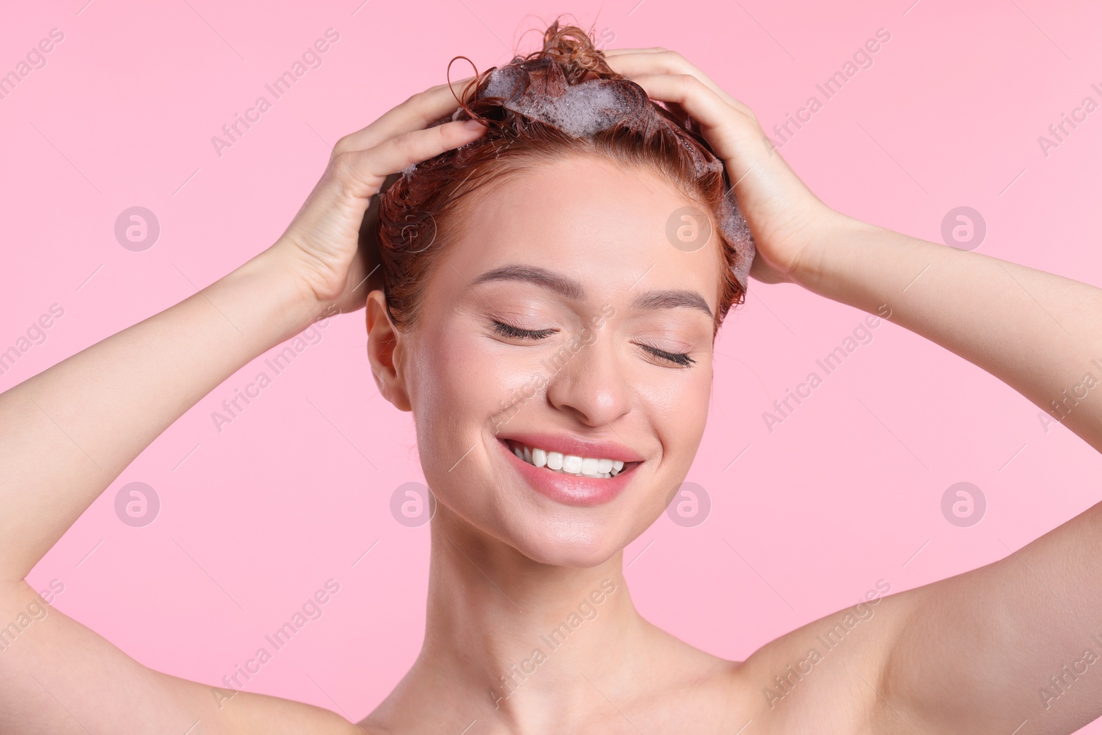 Photo of Happy young woman washing her hair with shampoo on pink background