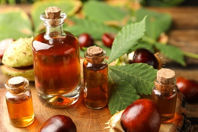 Photo of Chestnuts and bottles of essential oil on wooden table, closeup