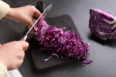 Woman cutting fresh red cabbage at black table, closeup