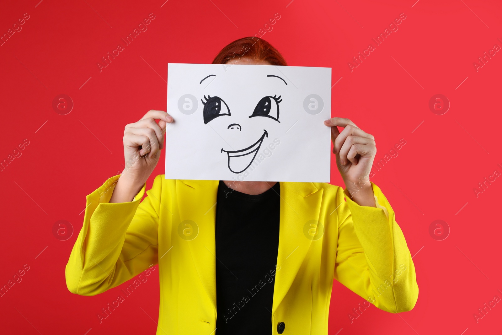 Photo of Woman hiding behind sheet of paper with happy face on red background