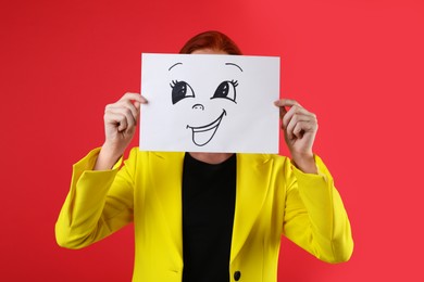 Woman hiding behind sheet of paper with happy face on red background