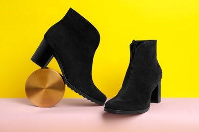 Photo of Stylish black female boots and decor on pink paper against yellow background