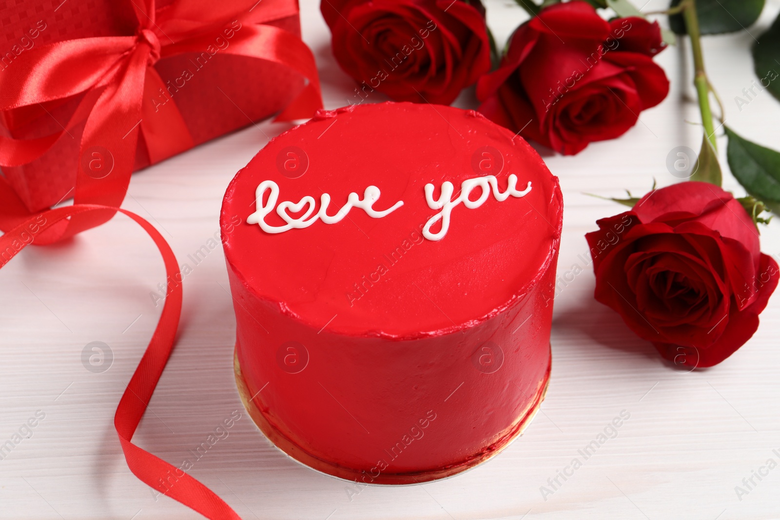 Photo of Bento cake with text Love You, gift box and roses on white wooden table. St. Valentine's day surprise