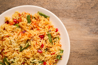 Photo of Tasty rice pilaf with vegetables on wooden table, top view