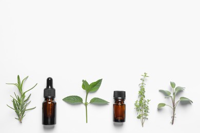 Bottles of essential oils and different herbs on white background, flat lay. Space for text