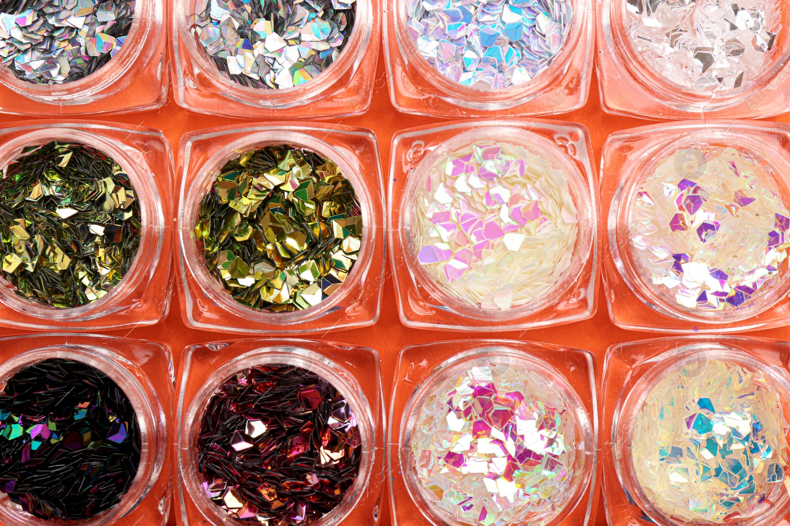 Photo of Jars with colorful shiny glitter on orange background, flat lay