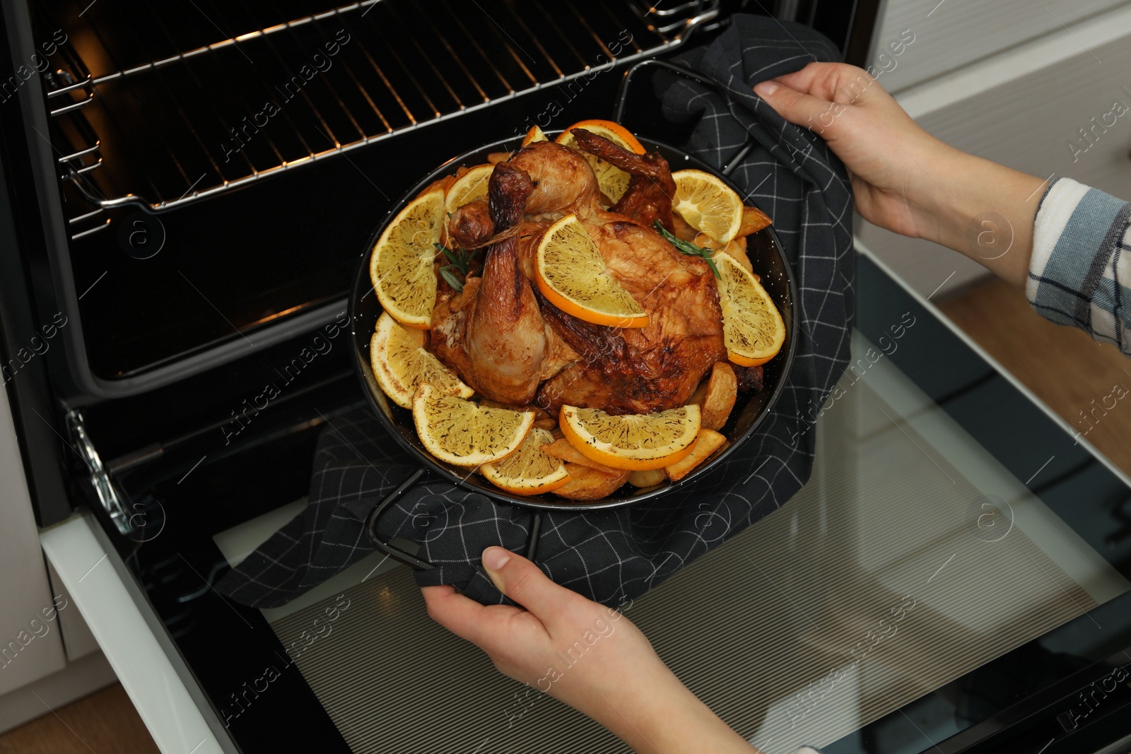 Photo of Woman taking baked chicken with orange slices out of oven, closeup