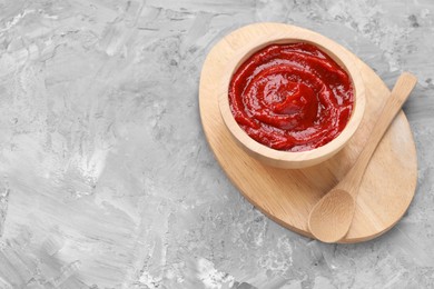 Photo of Organic ketchup in wooden bowl and spoon on grey textured table, above view with space for text. Tomato sauce
