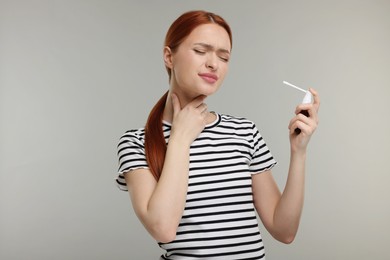 Young woman holding throat spray on grey background