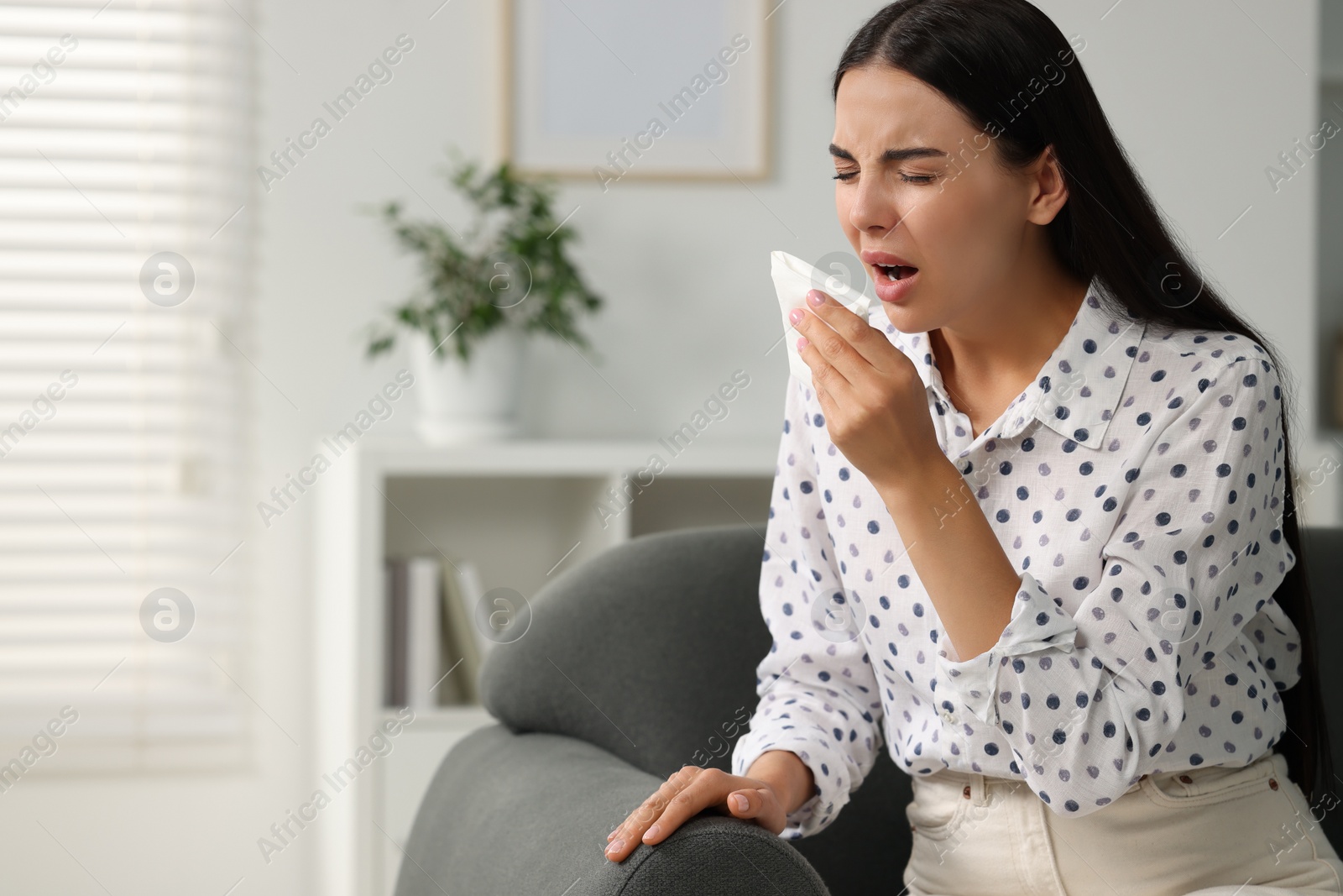 Photo of Suffering from allergy. Young woman with tissue sneezing at home, space for text