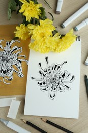 Drawings of chrysanthemum with flowers and art supplies on wooden table, flat lay