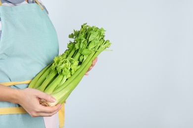 Woman holding fresh green celery on light background, closeup. Space for text