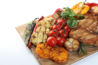 Photo of Wooden board with tasty grilled vegetables, meat, rosemary and basil isolated on white