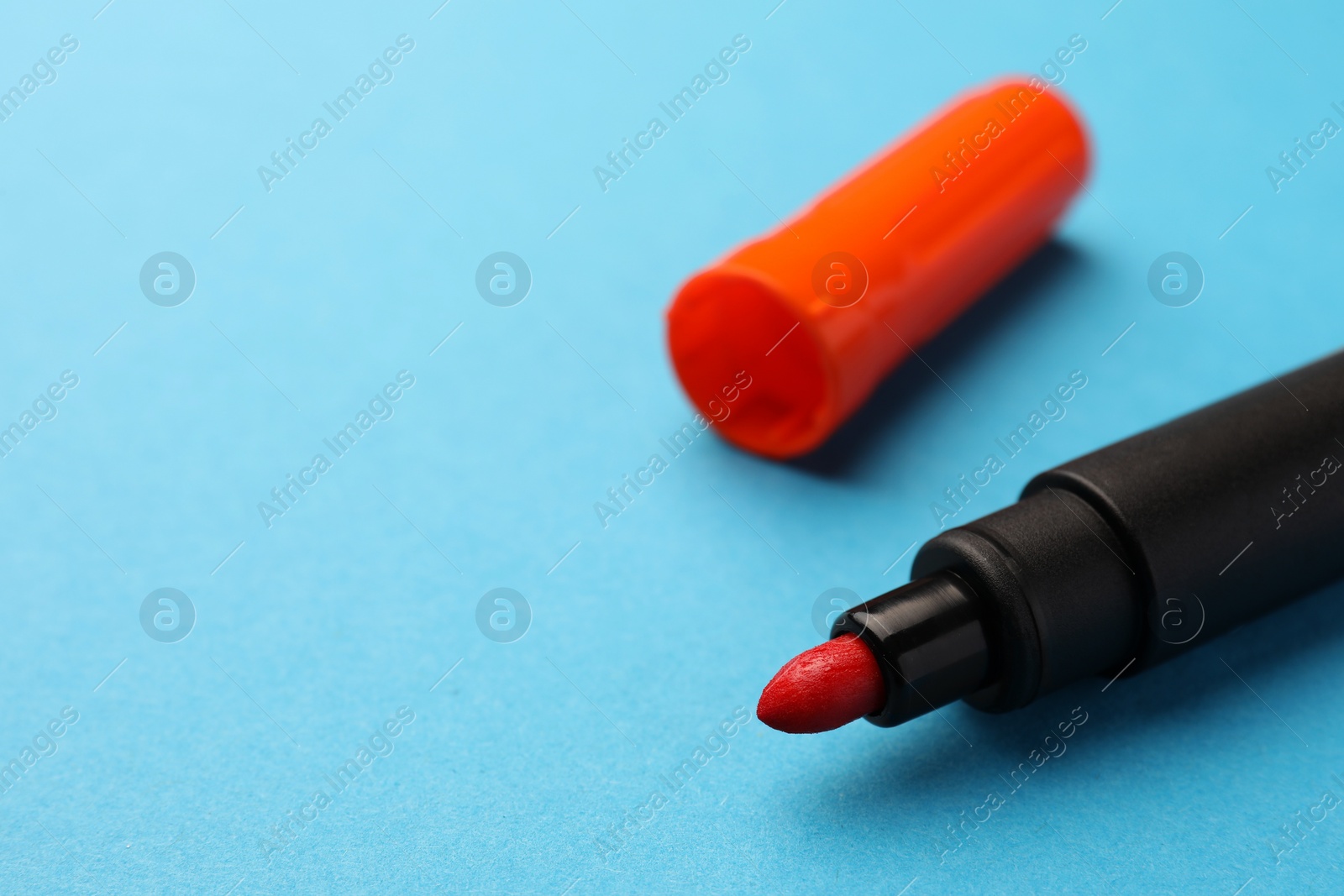 Photo of Bright orange marker on light blue background, closeup. Space for text