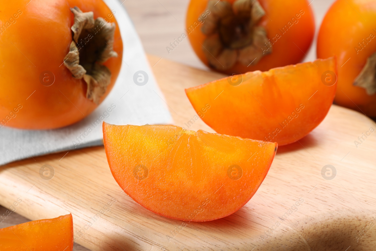 Photo of Delicious ripe persimmons on wooden board, closeup