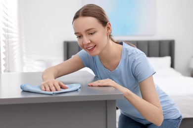 Photo of Woman with microfiber cloth cleaning grey chest of drawers in room