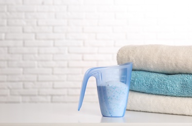 Photo of Measuring cup with washing powder and clean towels on table against brick wall, space for text. Laundry day