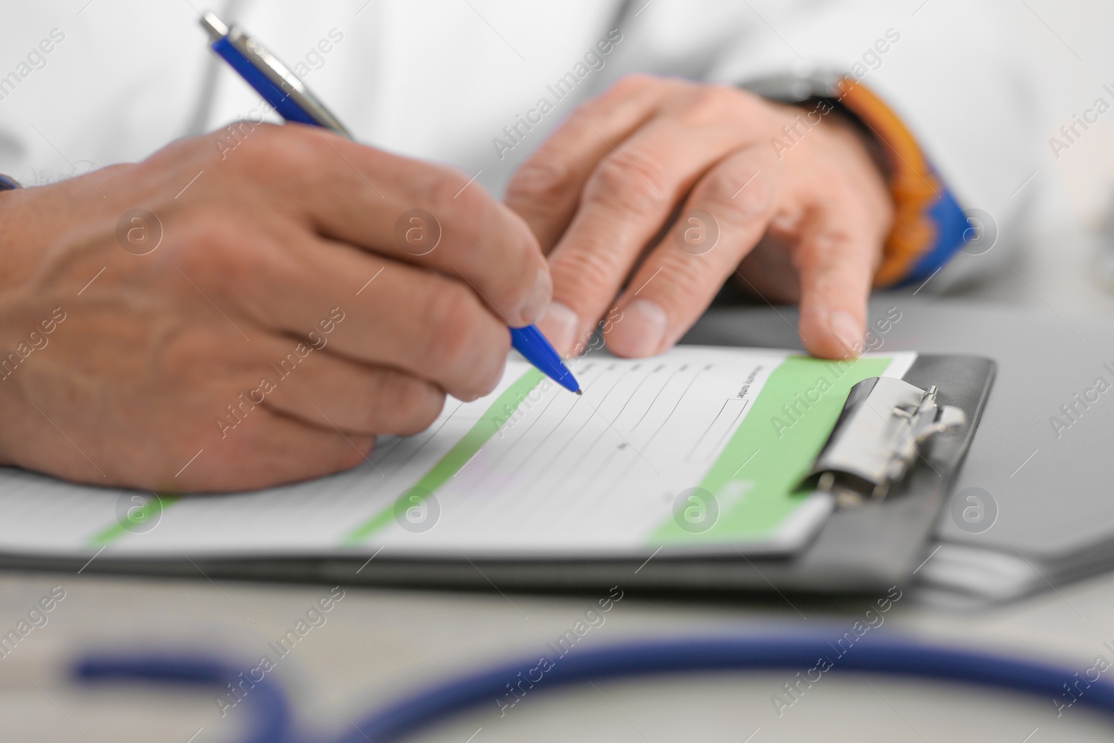 Photo of Doctor filling patient's medical card at table in clinic, closeup