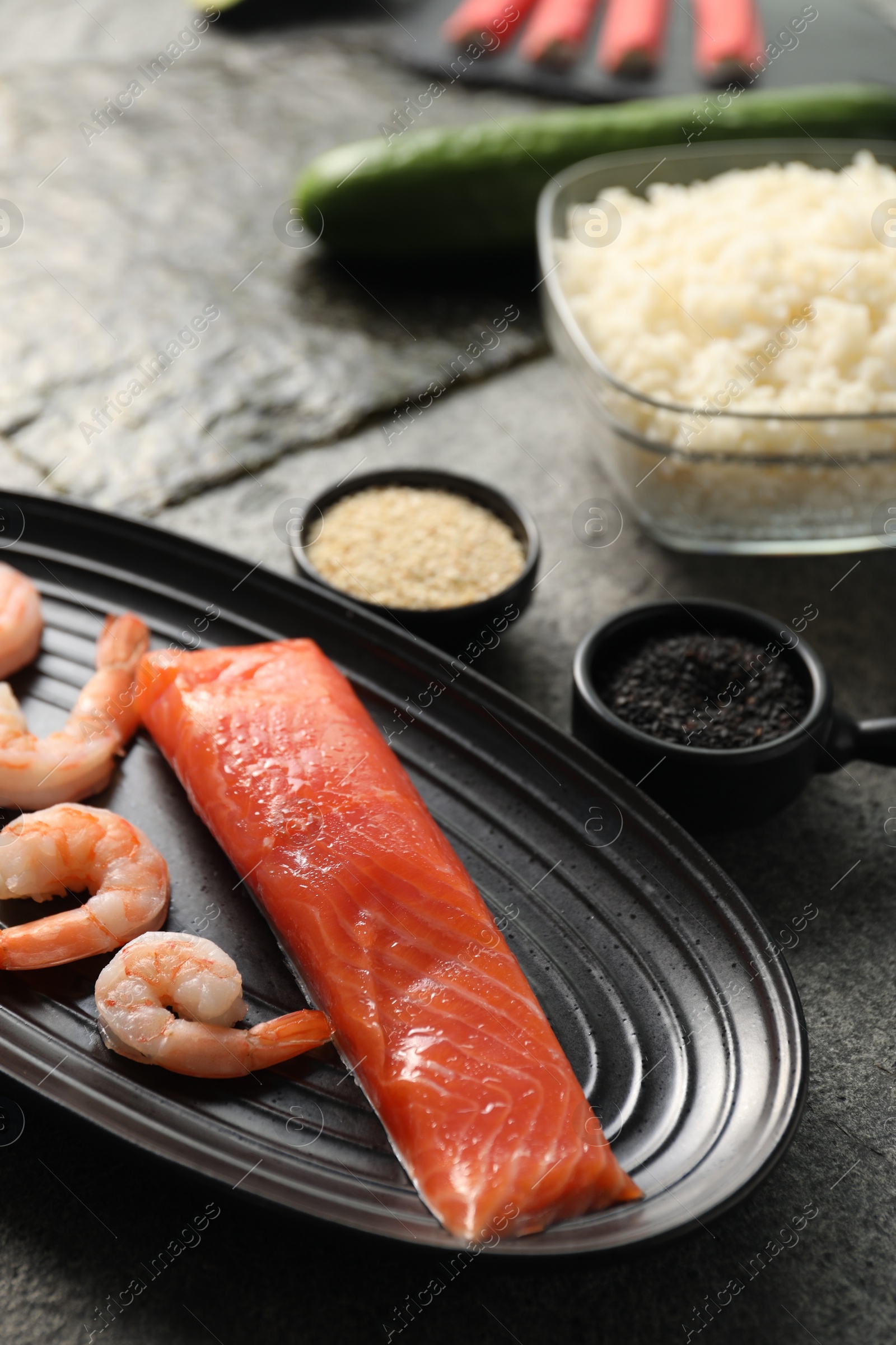 Photo of Fresh salmon, shrimps and other ingredients for sushi on dark table, closeup