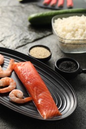 Photo of Fresh salmon, shrimps and other ingredients for sushi on dark table, closeup