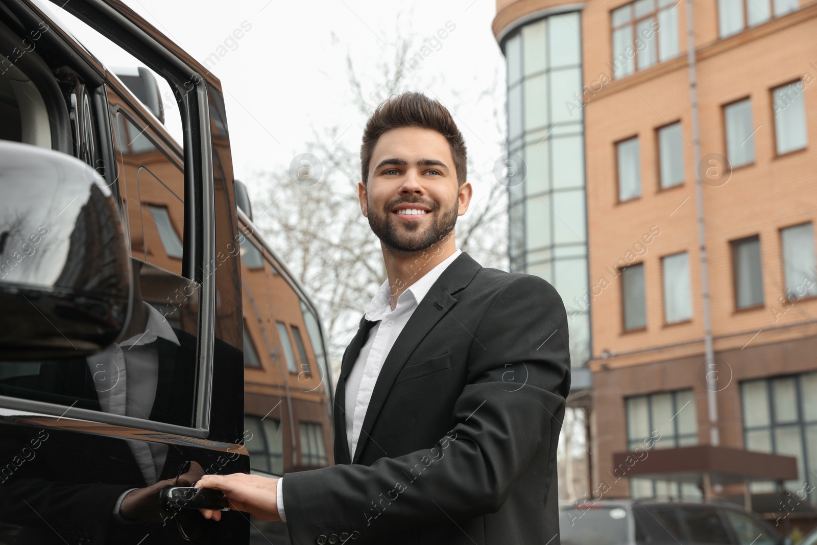 Photo of Handsome young man opening door of modern car outdoors