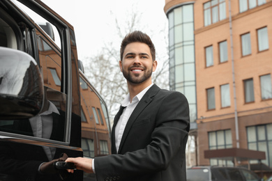 Handsome young man opening door of modern car outdoors