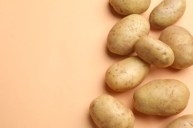 Photo of Fresh raw potatoes on pale orange background, flat lay. Space for text