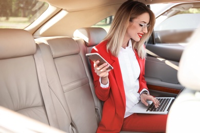 Photo of Young businesswoman with smartphone and laptop in car