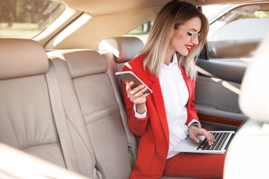 Young businesswoman with smartphone and laptop in car