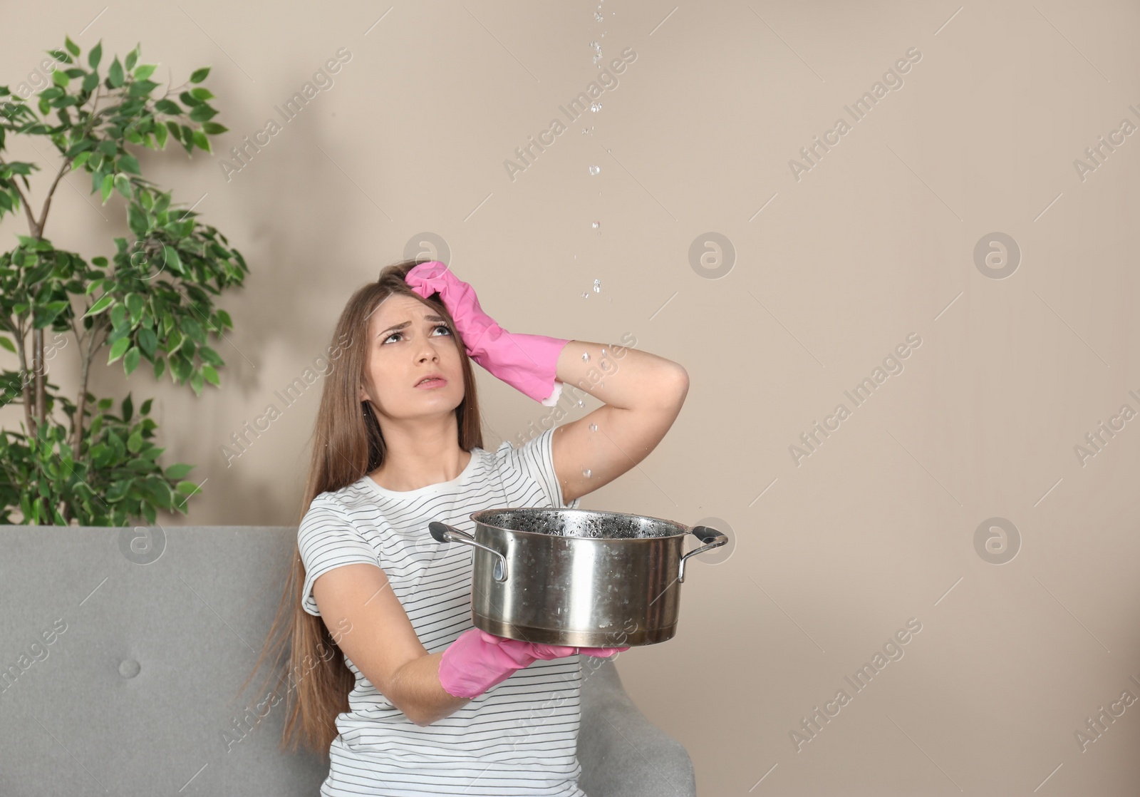 Photo of Worried young woman collecting water leakage from ceiling at home. Time to call plumber