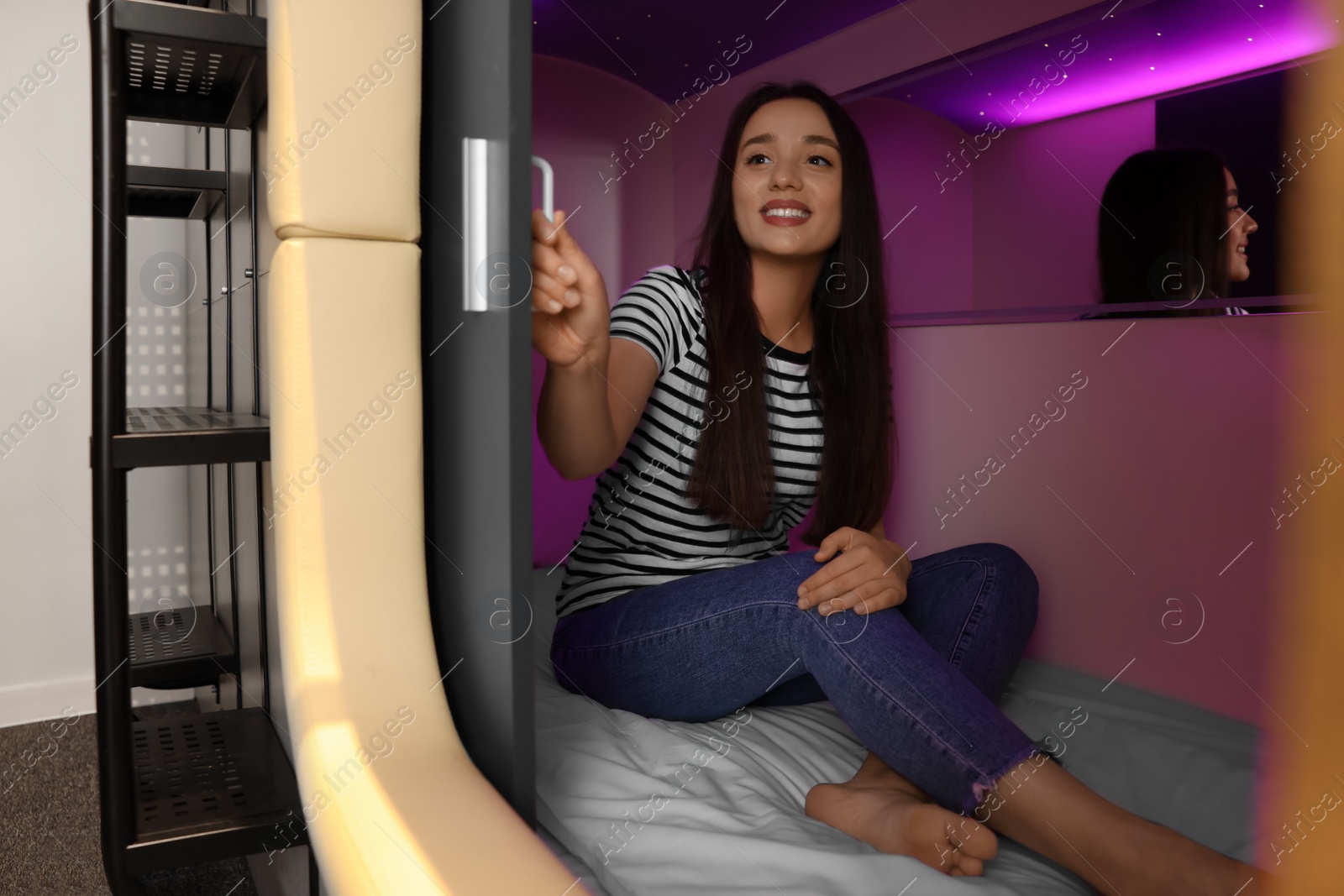 Photo of Happy young woman closing door of capsule in pod hostel