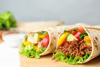 Board with delicious meat tortilla wraps on white wooden table, closeup