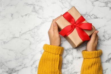 Photo of Young woman holding Christmas gift on white marble background, top view. Space for text