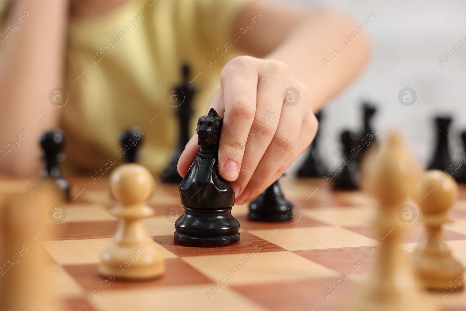 Photo of Little child playing chess indoors, closeup view