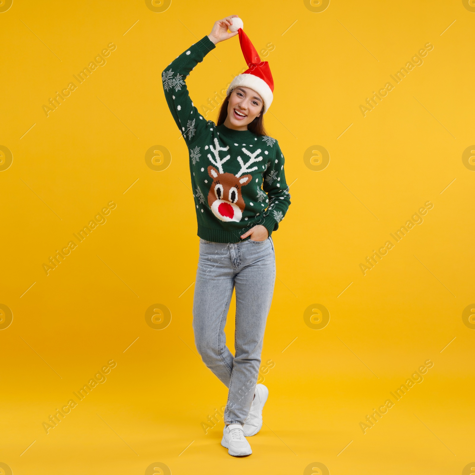 Photo of Happy young woman in Christmas sweater and Santa hat on orange background