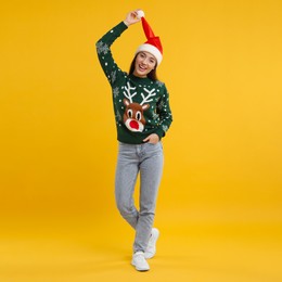 Photo of Happy young woman in Christmas sweater and Santa hat on orange background