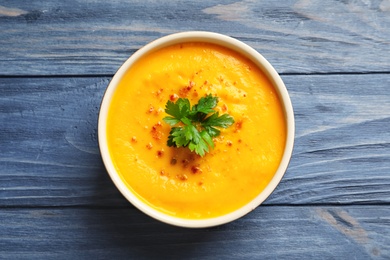 Delicious pumpkin cream soup in bowl on wooden background, top view