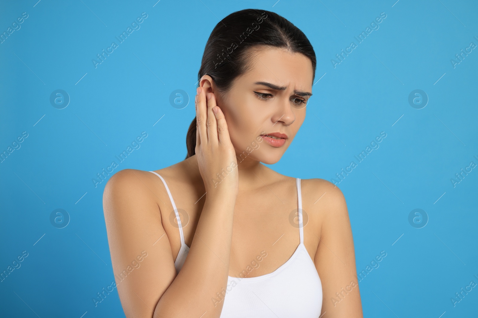 Photo of Young woman suffering from ear pain on light blue background