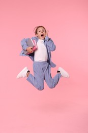 Photo of Happy schoolgirl with books jumping on pink background