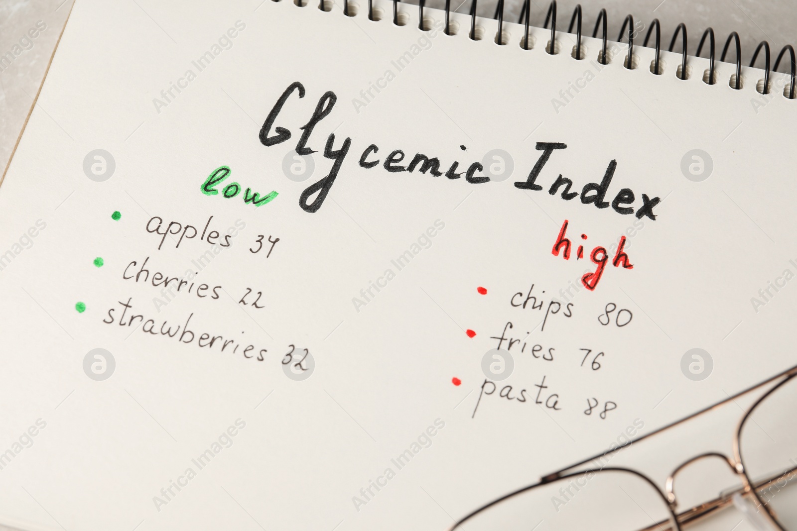 Photo of List with products of low and high glycemic index in notebook on table, closeup