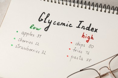 List with products of low and high glycemic index in notebook on table, closeup